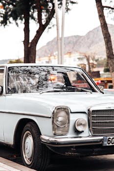 Classic white vintage car parked outdoors with scenic mountain background and trees.