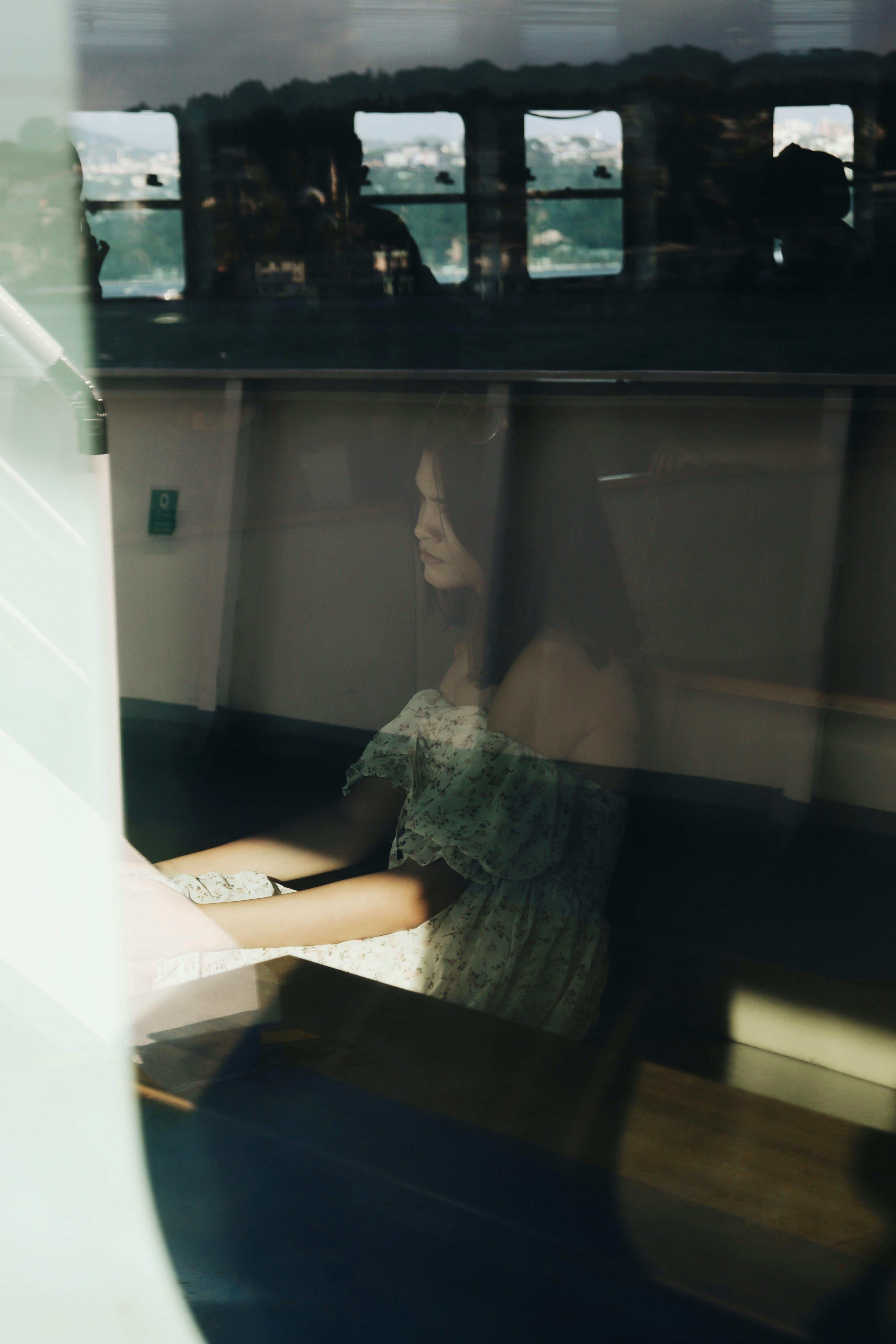 A young woman sits reflectively by a train window, traveling during the day.