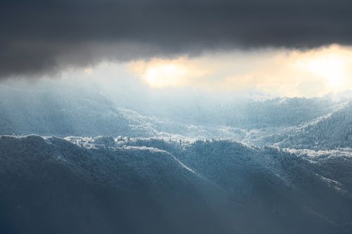 Free A breathtaking view of snow-covered mountains with dramatic clouds and sunlight filtering through, creating a mystical atmosphere. Stock Photo