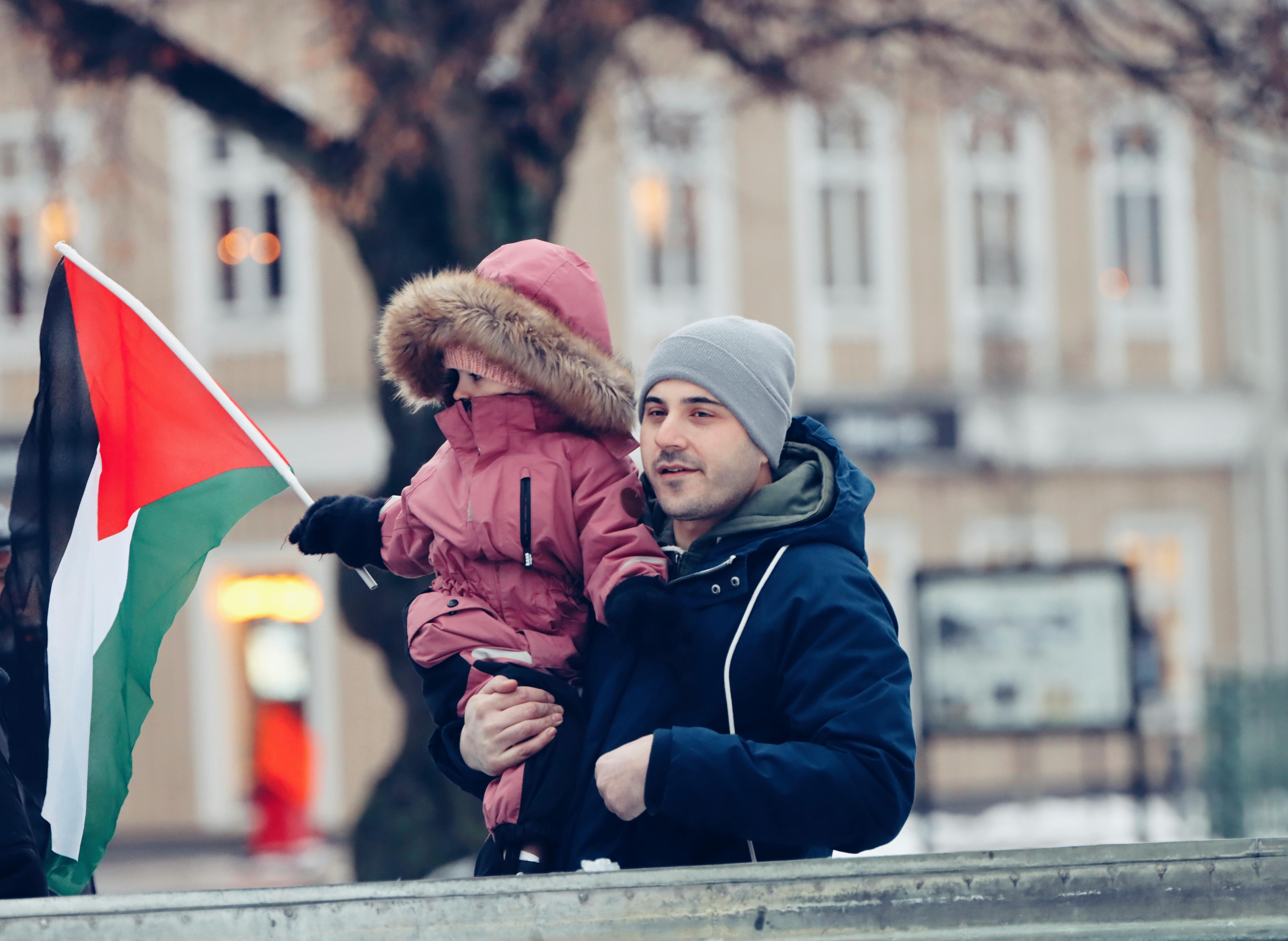 A father and child in winter clothing holding a flag in Jönköping, Sweden, urban setting.