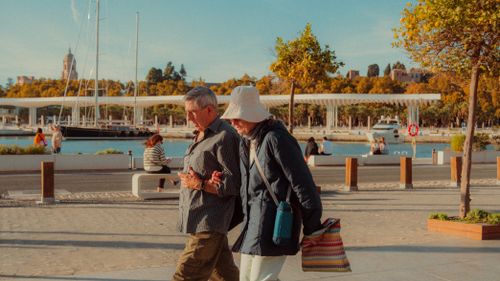 Free Senior couple walks arm in arm along the sunny promenade in Málaga, Spain. Scenic urban backdrop. Stock Photo
