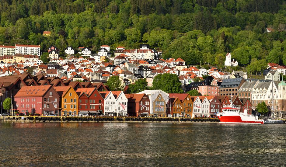 Scenic view of Bryggen's historic waterfront buildings in Bergen, Norway with lush green hills and a reflective harbor.