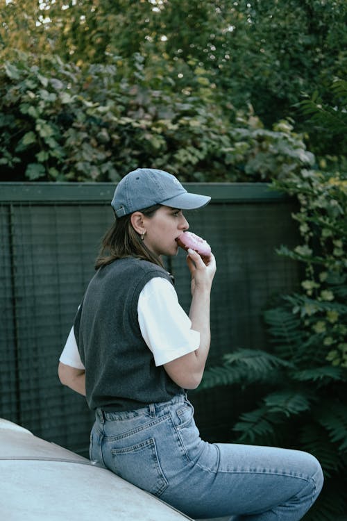 Brunette Woman with Cap Eating Pink Donut