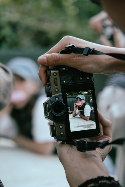 Photographer capturing a subject through a camera screen, showcasing hands and camera details.