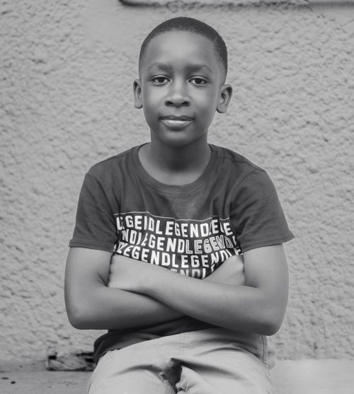 Free Monochrome portrait of a confident young boy with folded hands sitting against a textured wall. Stock Photo