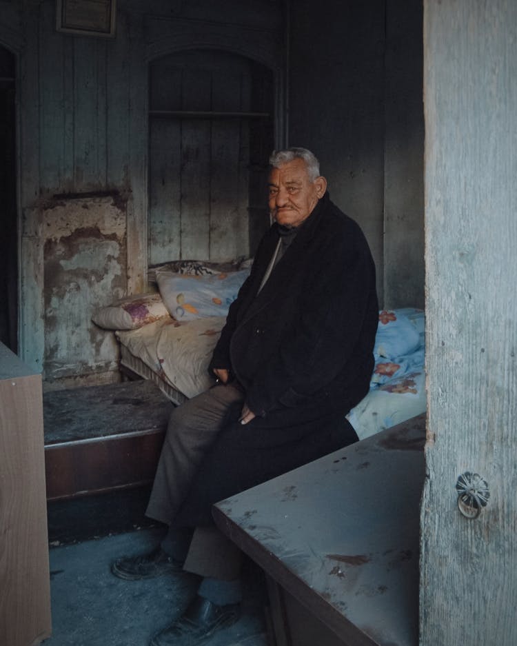 Man Sitting On Bed In Coat