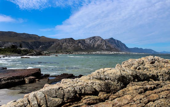 Breathtaking view of rocky coastline with mountains and sea in Hermanus, South Africa.