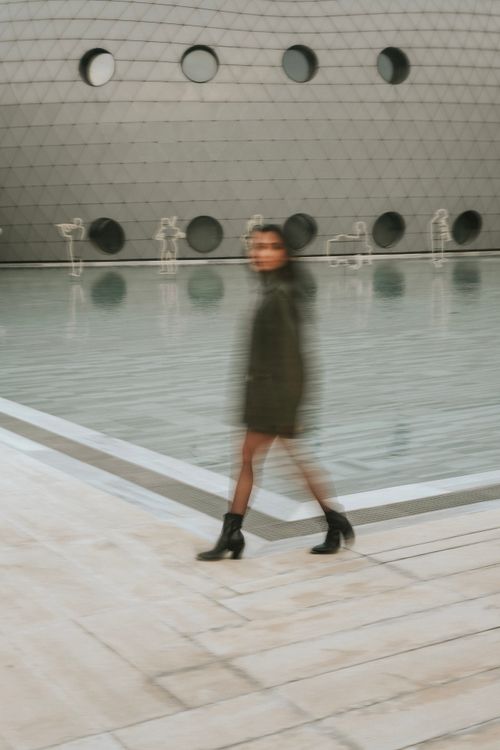 Free Blurred shot of a woman walking past a geometric building with circular windows. Stock Photo
