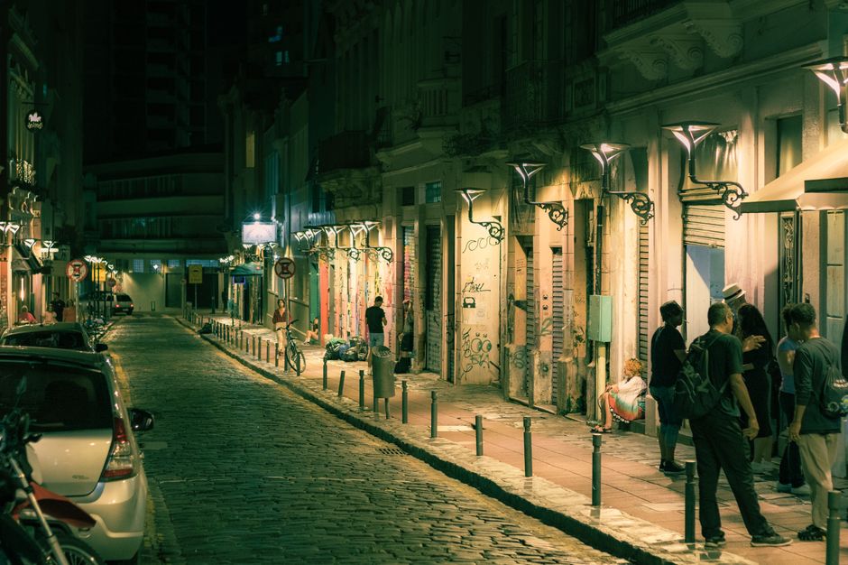 Explore the vibrant nightlife of a city street, illuminated by streetlights and bustling with people.
