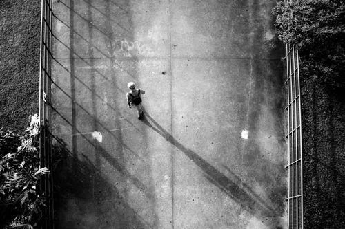 Free Overhead black and white view of a pedestrian on a city sidewalk casting a long shadow. Stock Photo