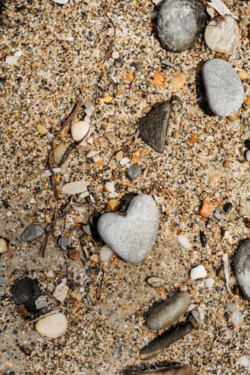 A heart shaped rock and pebbles on the sand