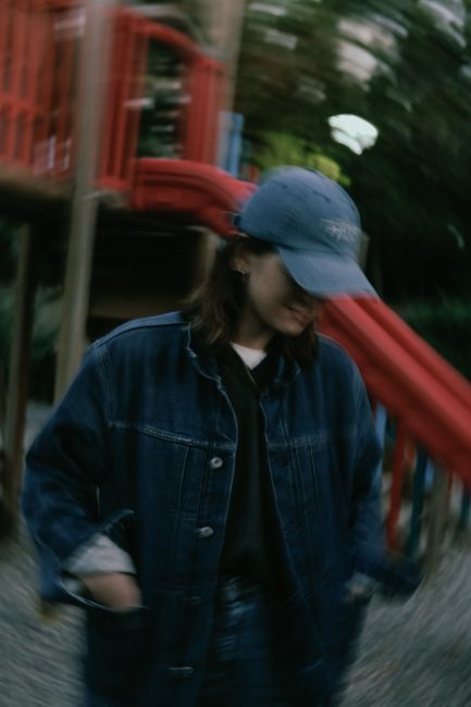Blurred portrait of a woman in a denim jacket and cap at a playground.