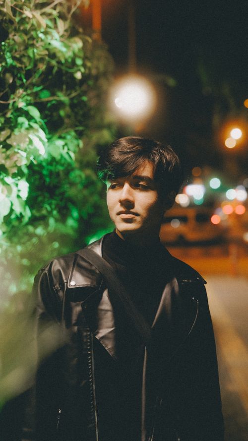 Free Portrait of a young man in a black leather jacket on a vibrant urban street at night. Stock Photo