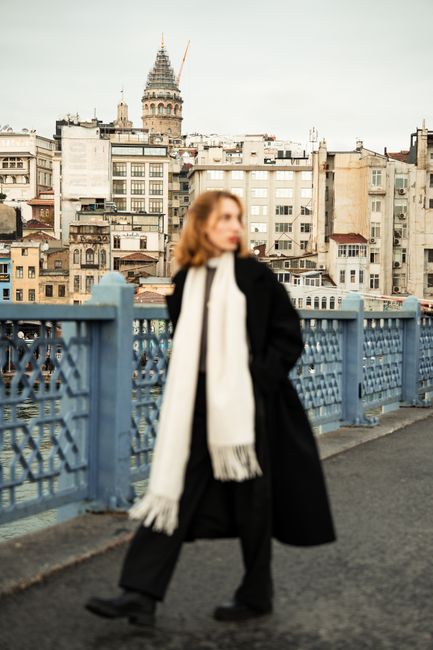 A woman in warm clothing walks on a bridge with a view of Istanbul's famous Galata Tower.