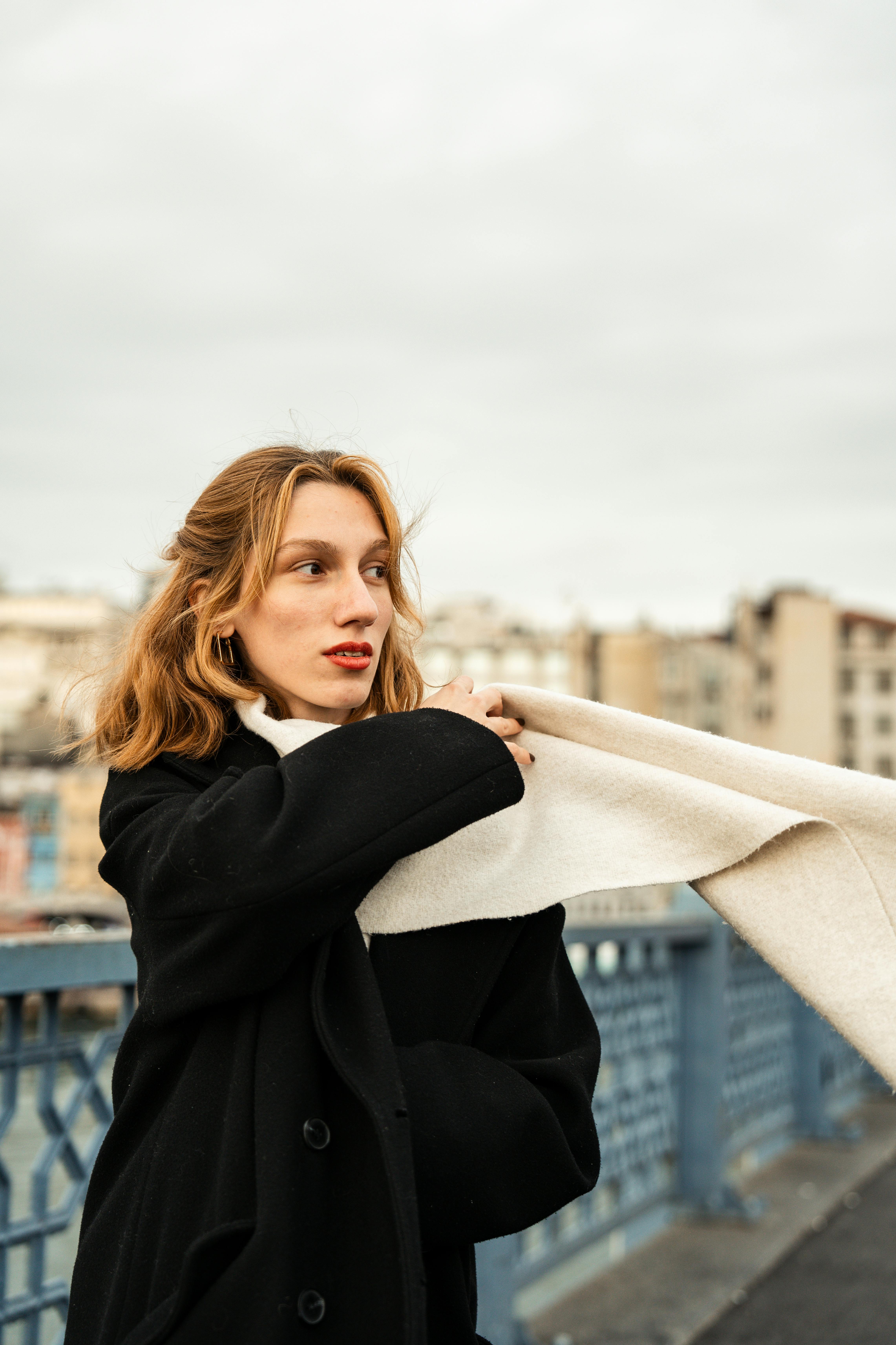 Elegant woman in black coat holding a scarf on a city bridge. Capturing urban fashion in a natural setting.