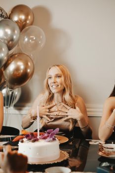 Woman enjoying a birthday celebration with balloons and a decorative cake, indoors.