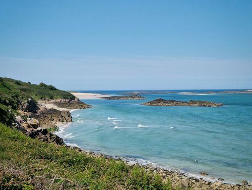 Free A beautiful coastal landscape with clear blue skies and gentle waves crashing on rocky shores. Stock Photo