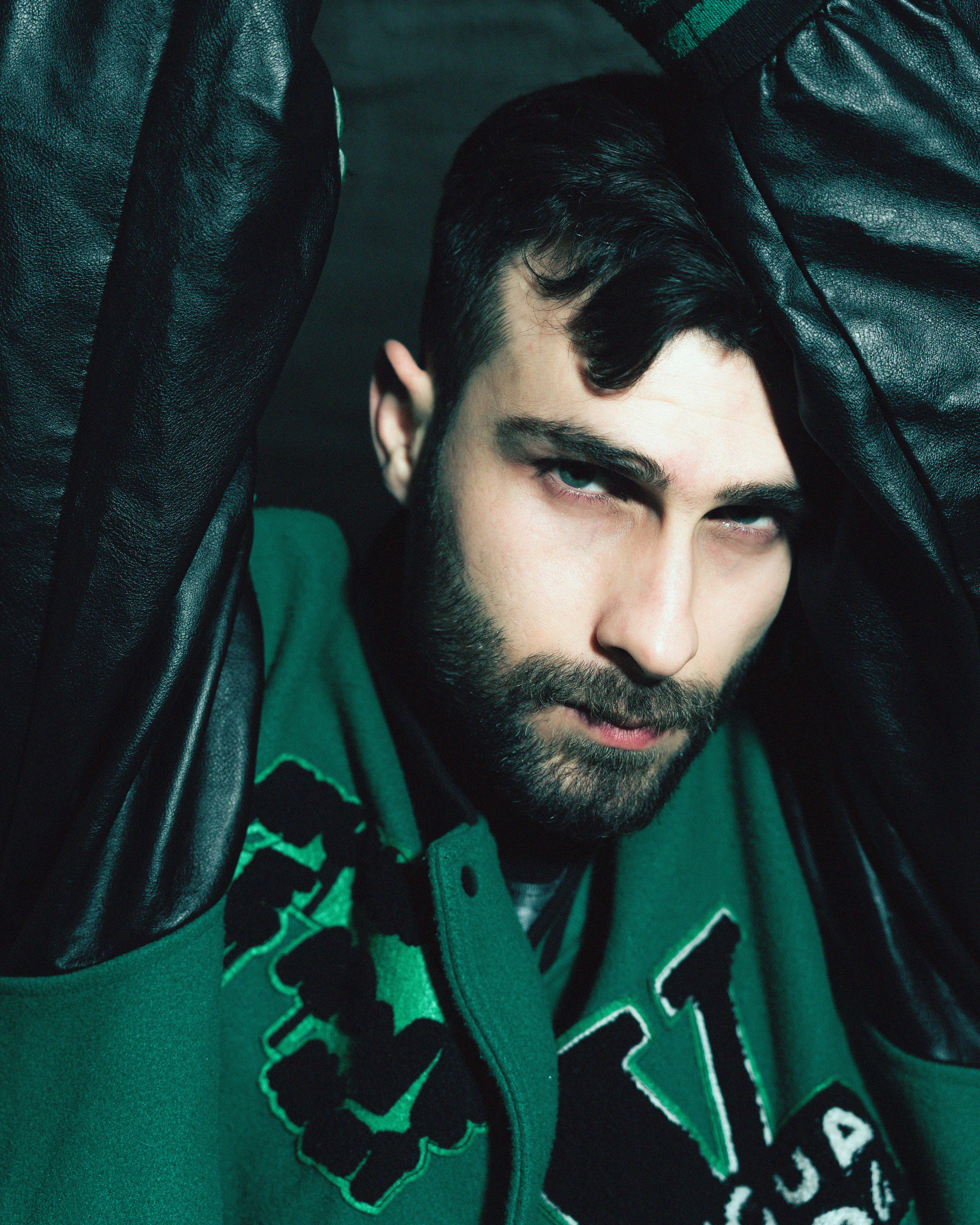 Close-up portrait of a bearded young man in a stylish jacket with a moody expression.