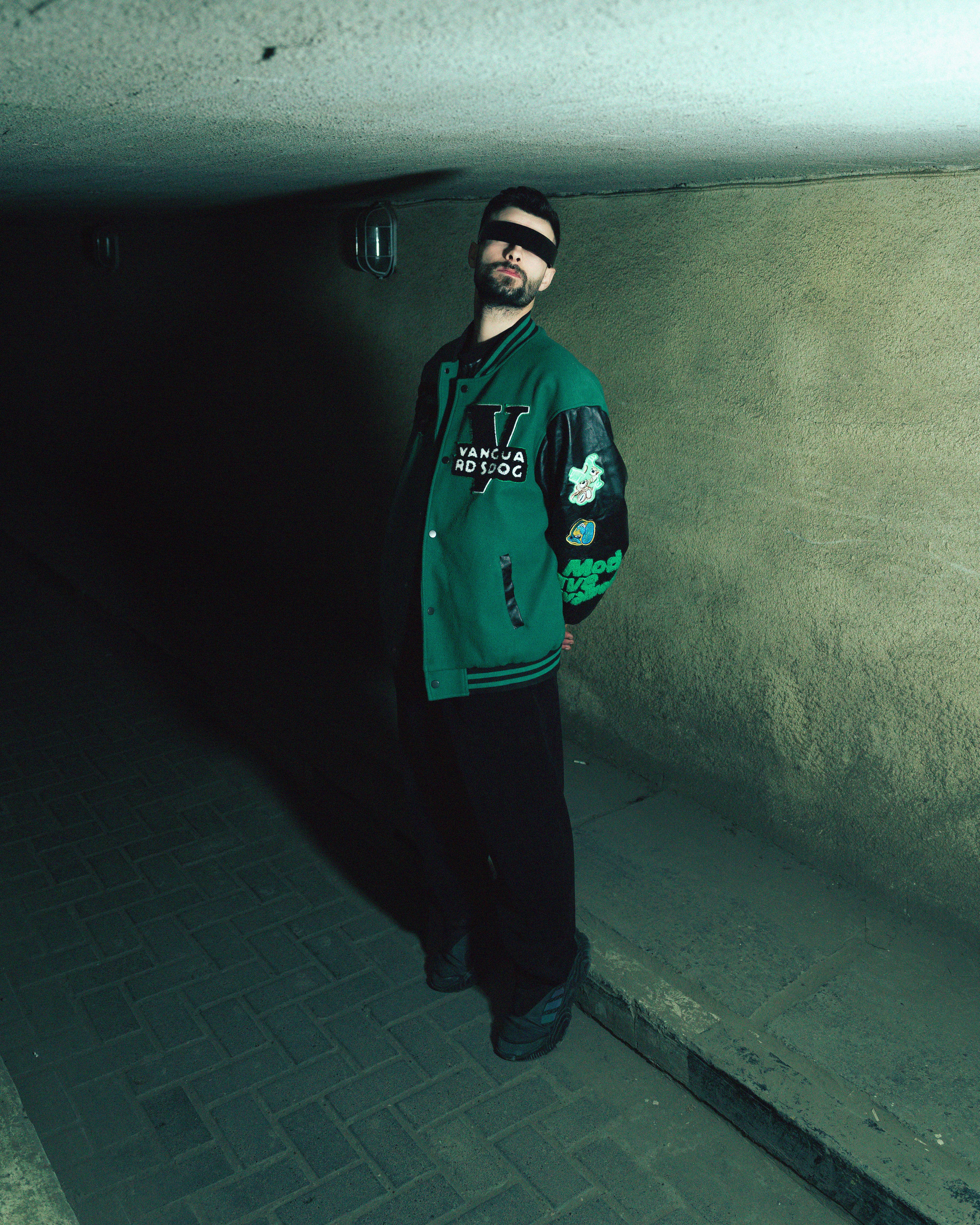 Man in trendy green jacket standing confidently in a dimly lit tunnel.