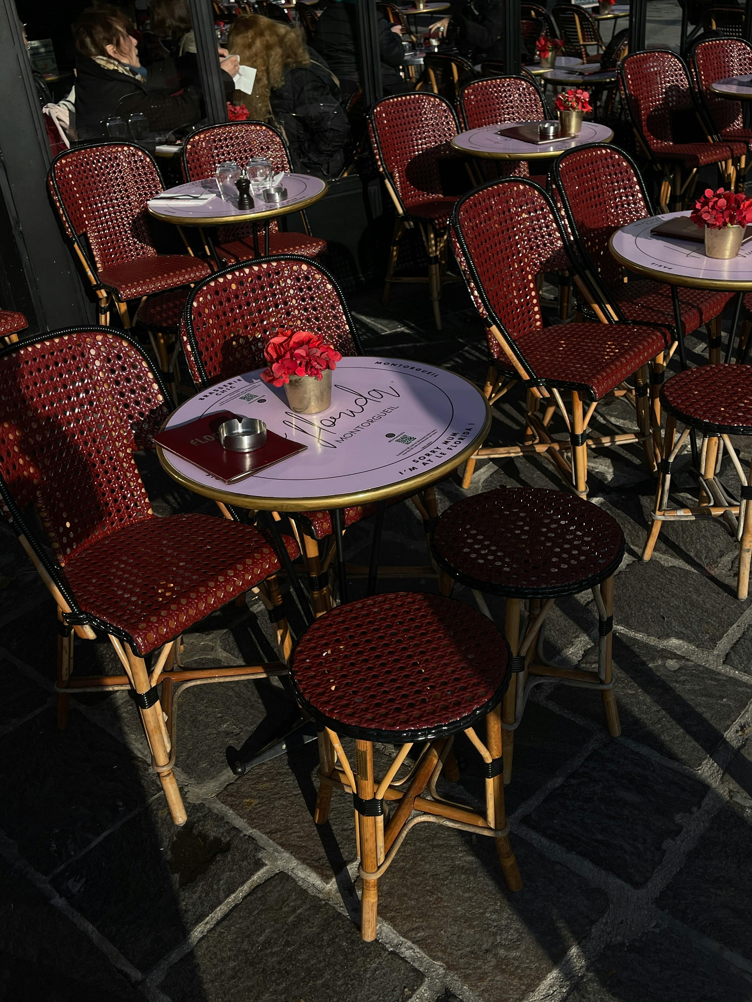 Outdoor café with red wicker chairs and round tables in a sunlit urban setting.