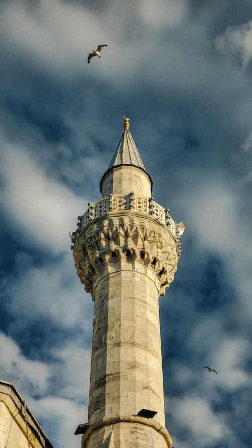 Free Vertical shot of an ornate mosque minaret with a dramatic blue sky and passing birds in Istanbul. Stock Photo