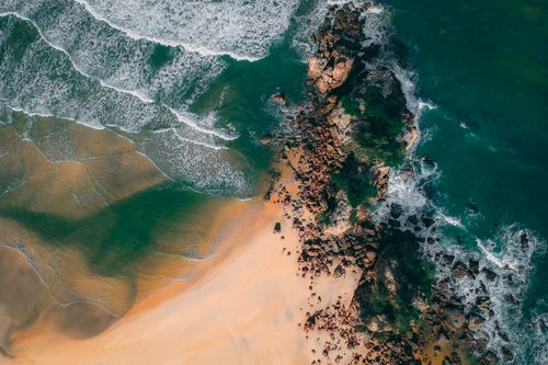Free Stunning aerial view of a rocky seashore with turquoise waters and sandy beach. Stock Photo