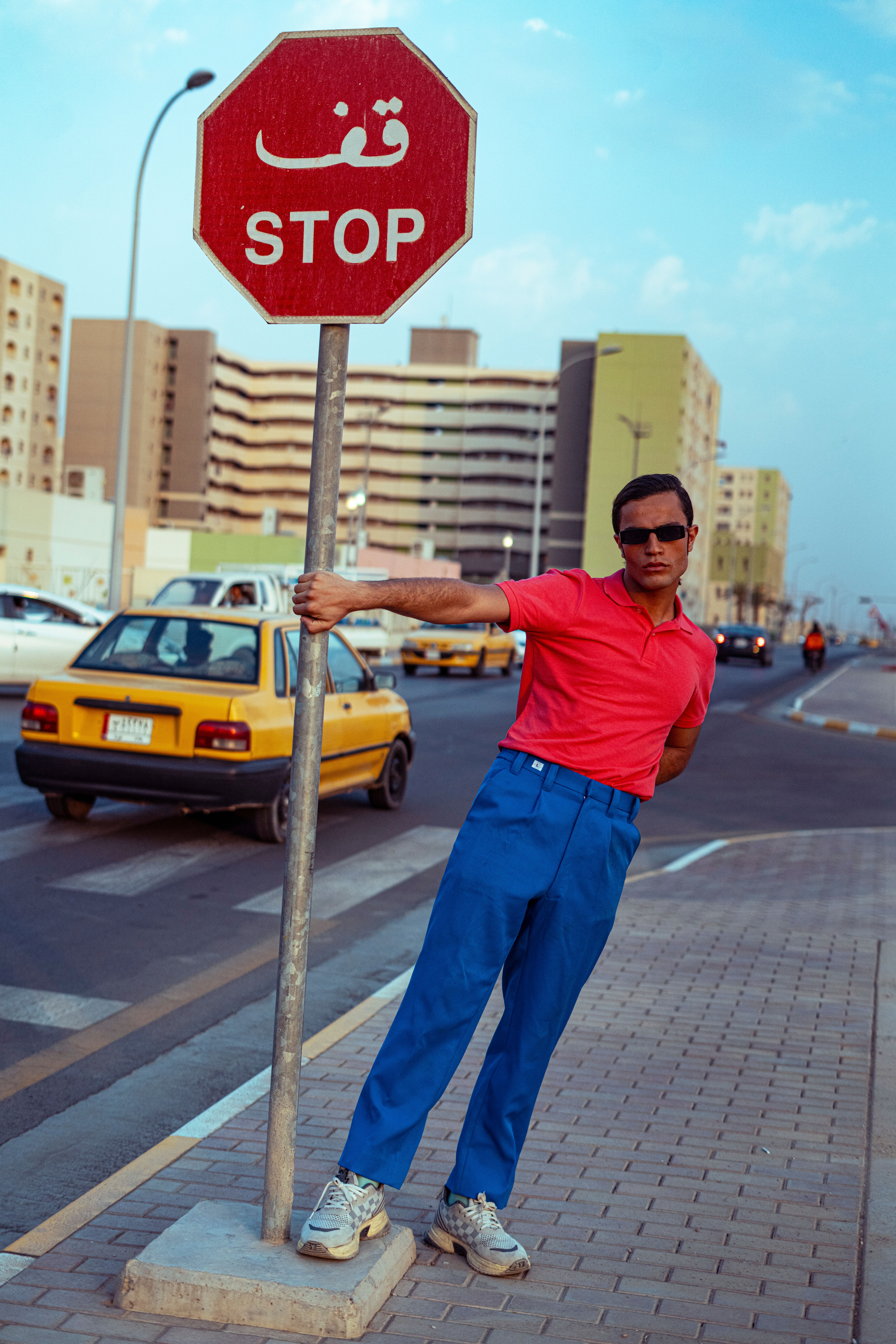 Man in sunglasses posing by stop sign on a city sidewalk in Iraq.