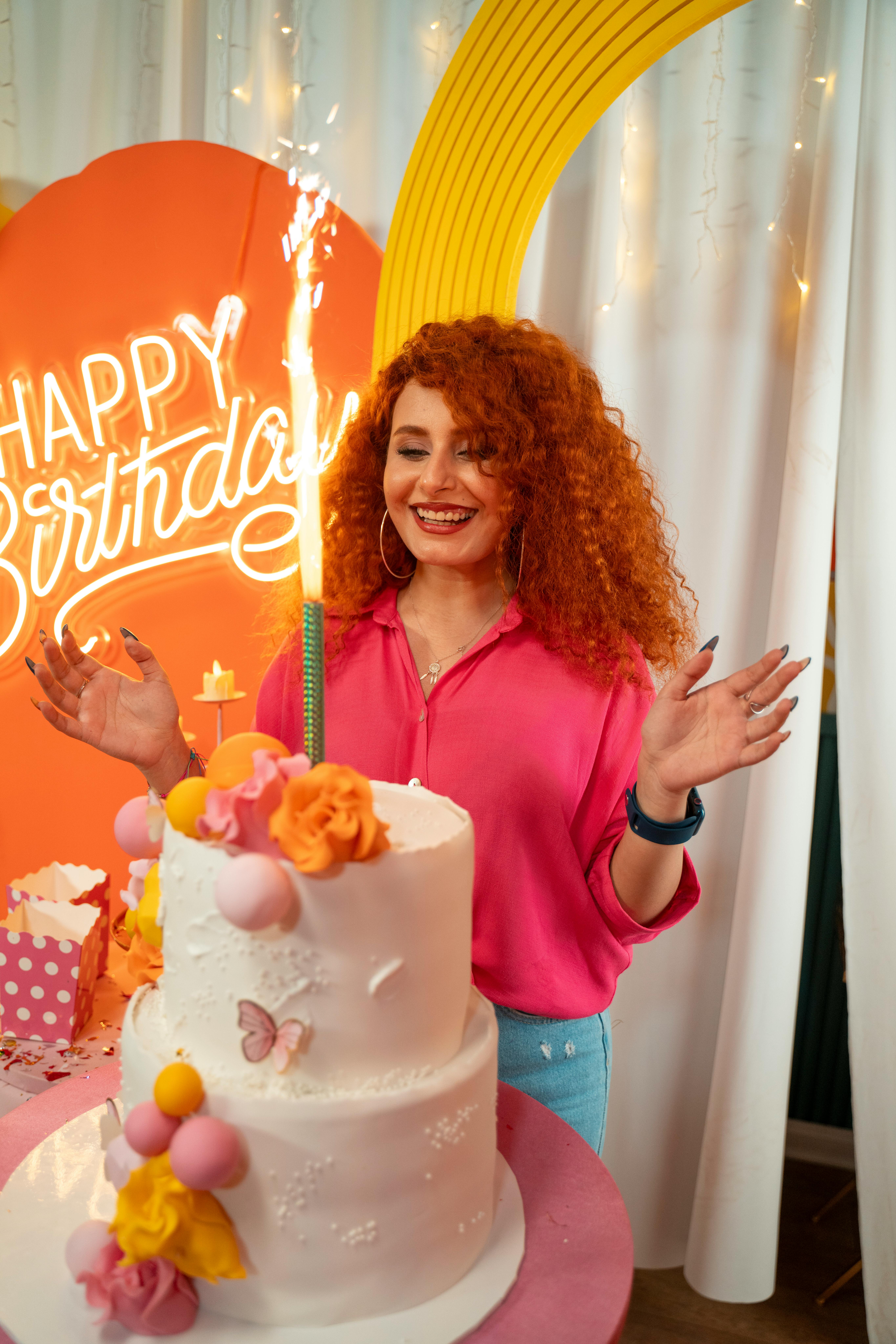 Young woman celebrates birthday with a vibrant cake and festive decor indoors.