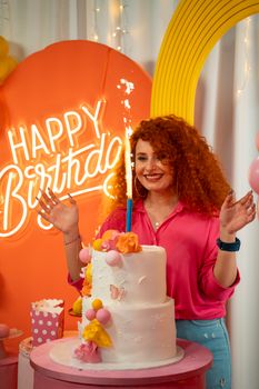 A woman enjoying a vibrant birthday party with a decorated cake and festive backdrop.