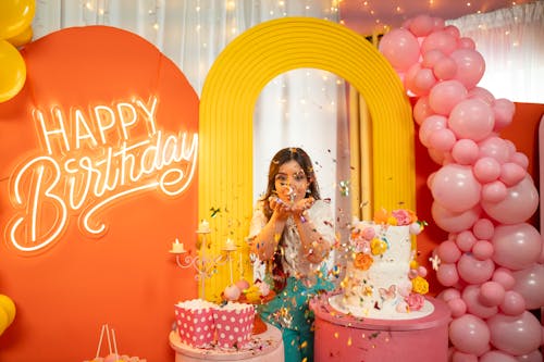 Young Woman Throwing Confetti between Birthday Decorations 