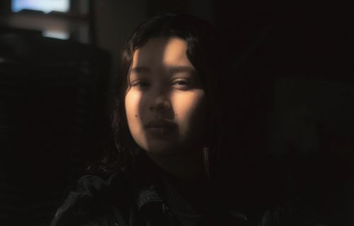 Free Artistic portrait of a teenager in a shadowy setting with soft light highlighting the face. Stock Photo