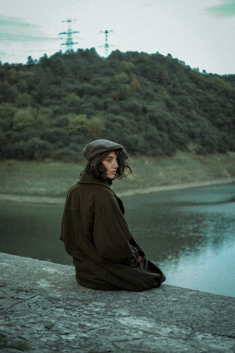 Brunette Woman In Coat Sitting By River