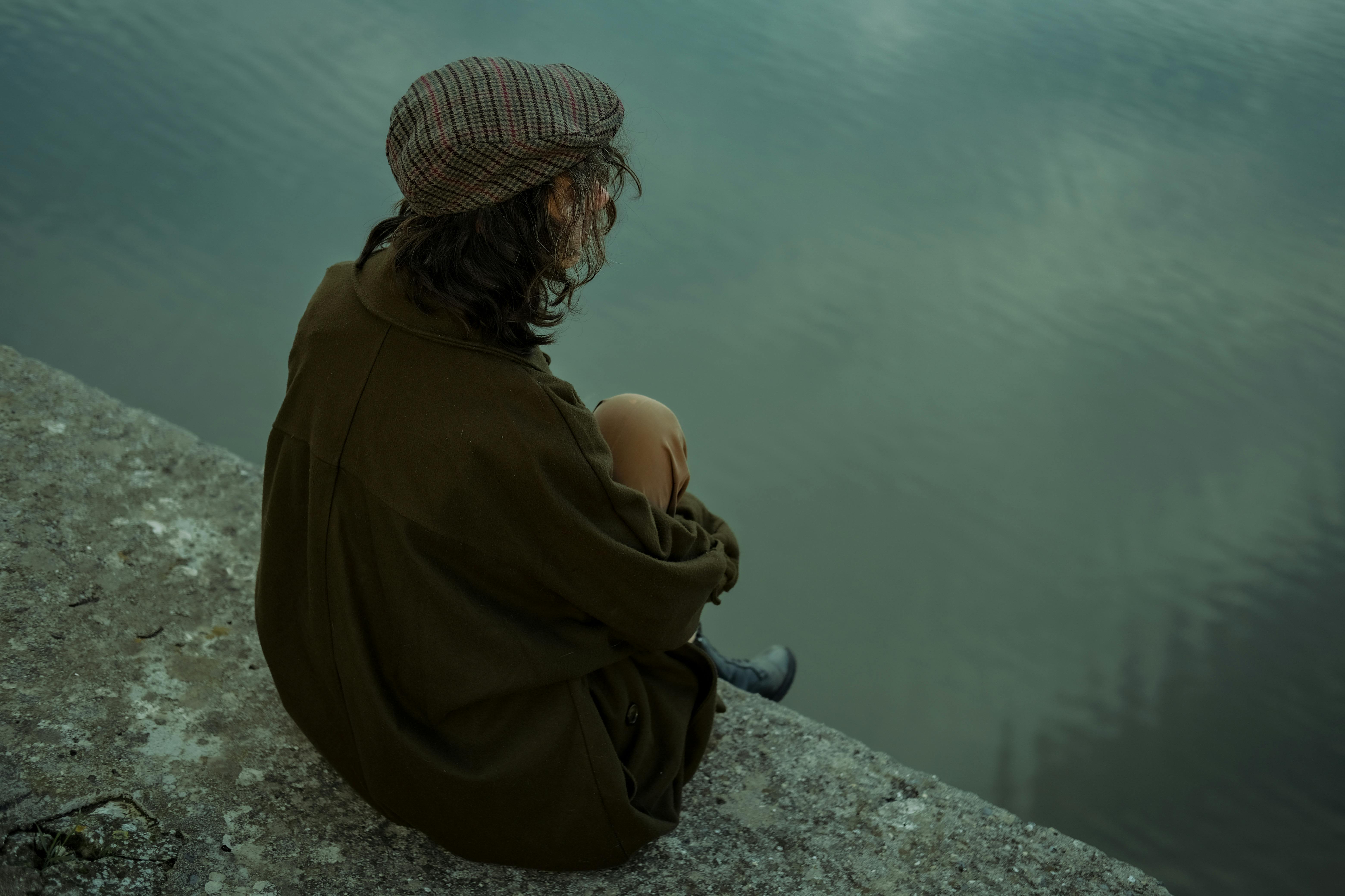 A woman sitting near a lake in contemplation, the identity-level depth work spiritual life coaching is designed for.