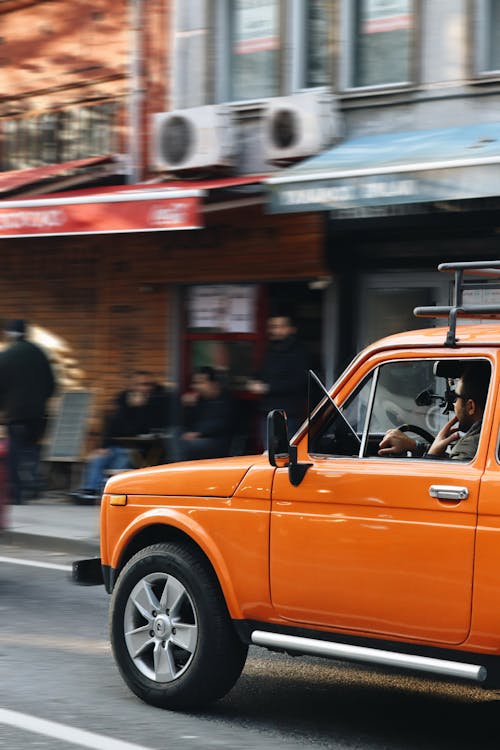 An Orange Car Driving on the Street in City 