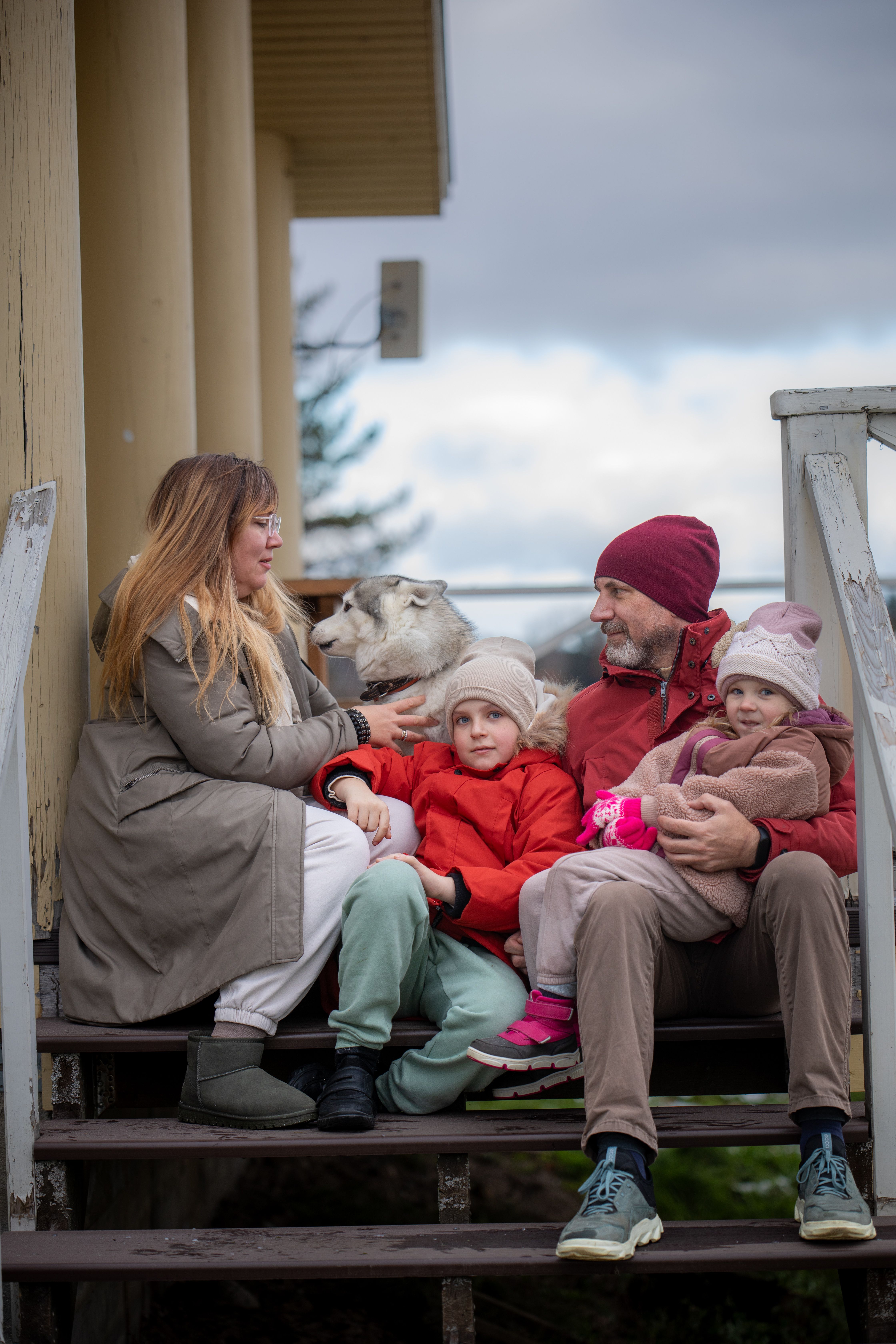 A family of four sitting on steps outdoors with their dog during winter, dressed in warm clothing.