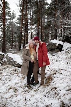 A couple wearing warm clothing sharing a joyful moment in a snowy forest. Perfect for winter lifestyle themes.