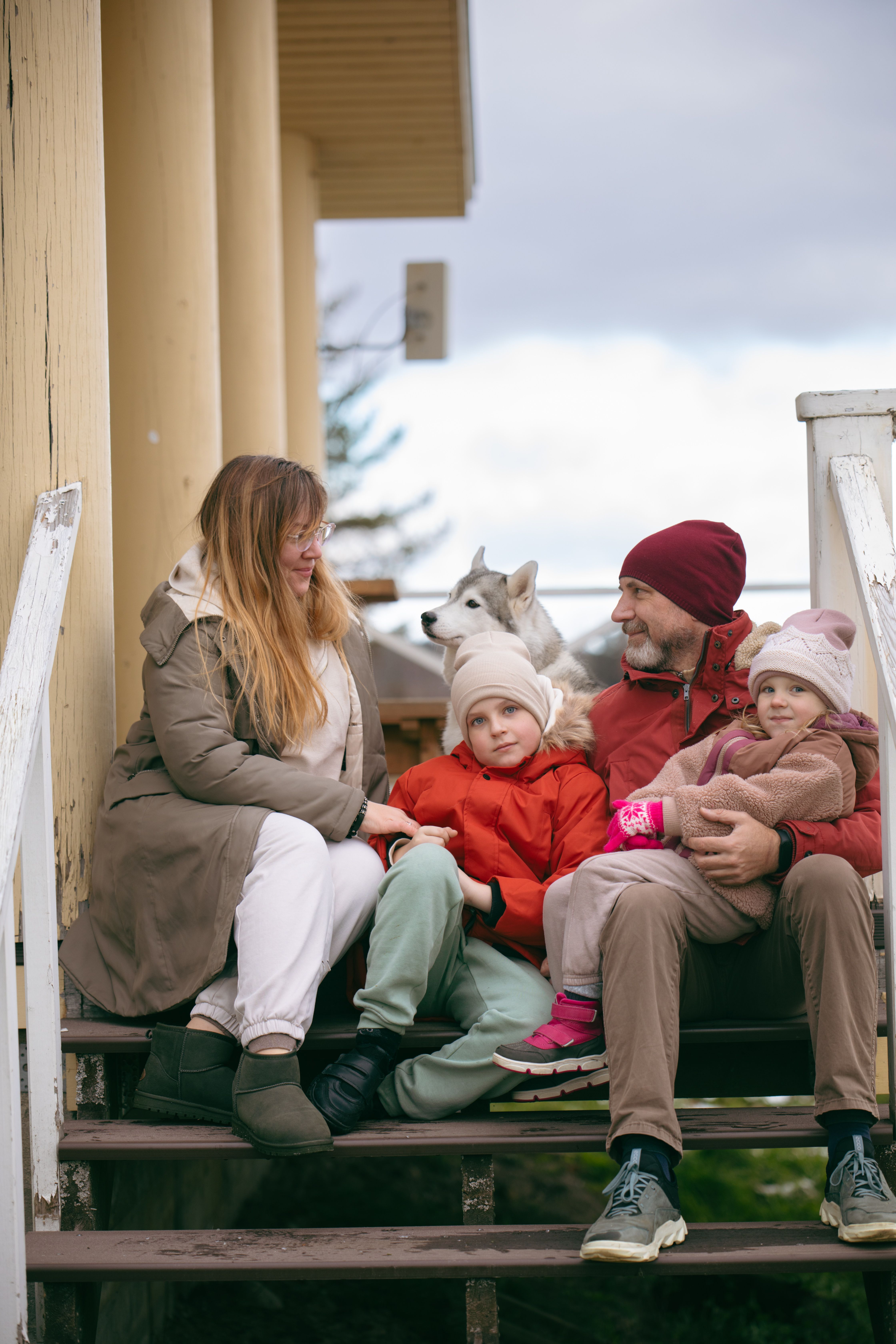A family with parents and children sitting on steps with their dog on a chilly day.