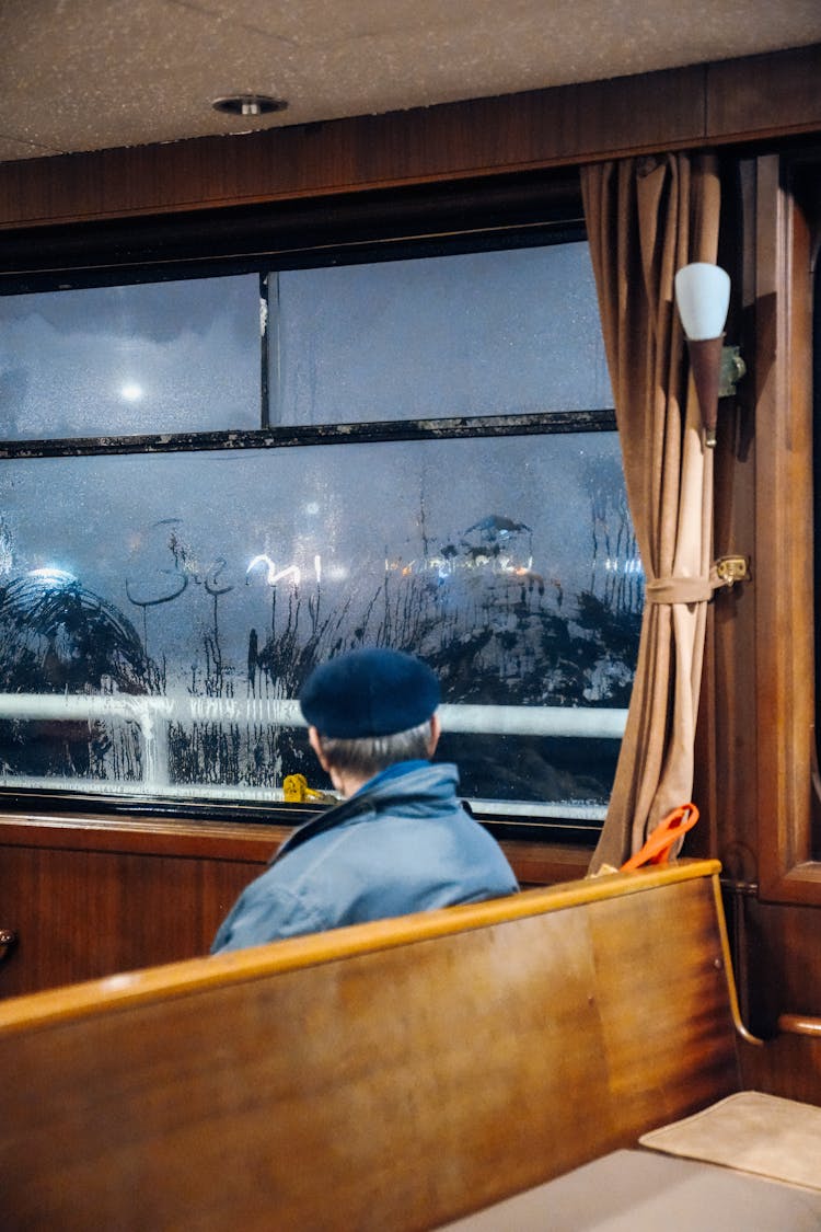 Man In Hat Sitting Near Window At Night