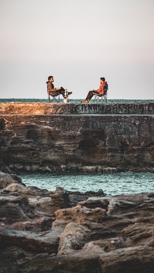 Men Sitting on Folding Chairs on a Shore 