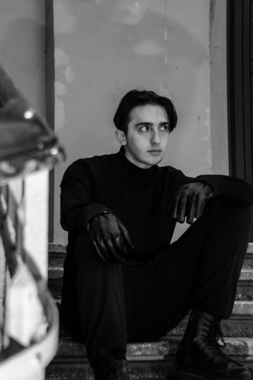 Free Black and white portrait of a man sitting on stairs wearing black attire. Stock Photo