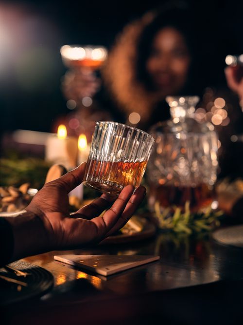 Free Hand holding whiskey glass during a festive night gathering with friends. Stock Photo