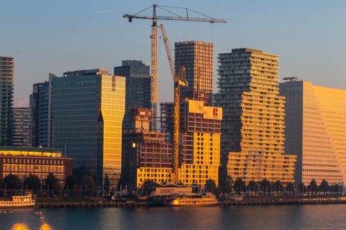 Free Skyscrapers and cranes along a riverfront skyline at dusk creating a modern urban landscape. Stock Photo
