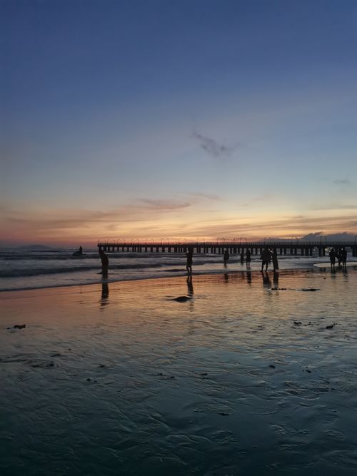 Free Silhouettes of people enjoying a serene sunset by the pier with calm ocean waves. Stock Photo