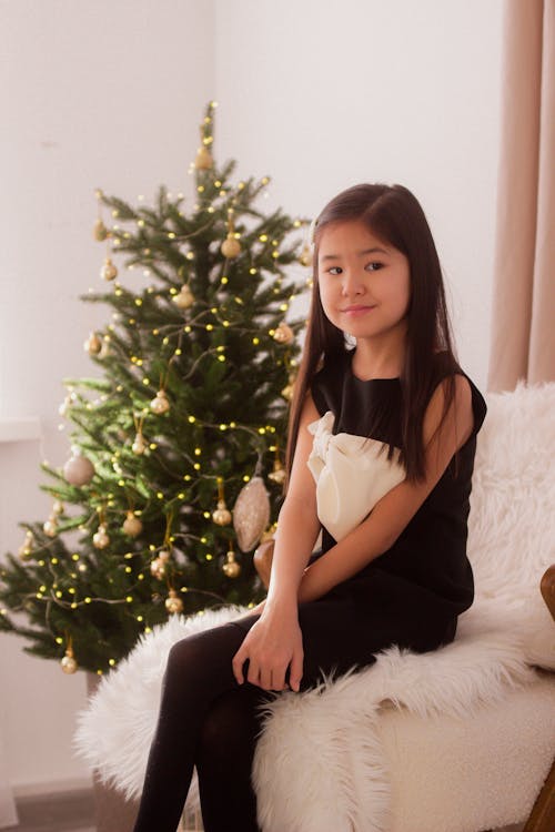 A Girl Sitting next to a Christmas Tree