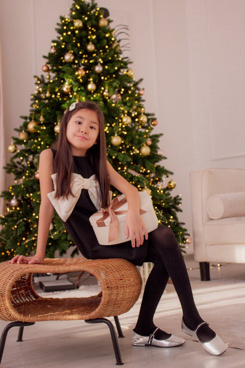 A Little Girl Sitting next to a Christmas Tree