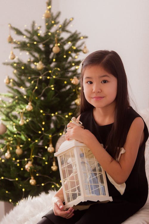 Portrait of a Little Girl Sitting in front of a Christmas Tree with a Lantern in Hands