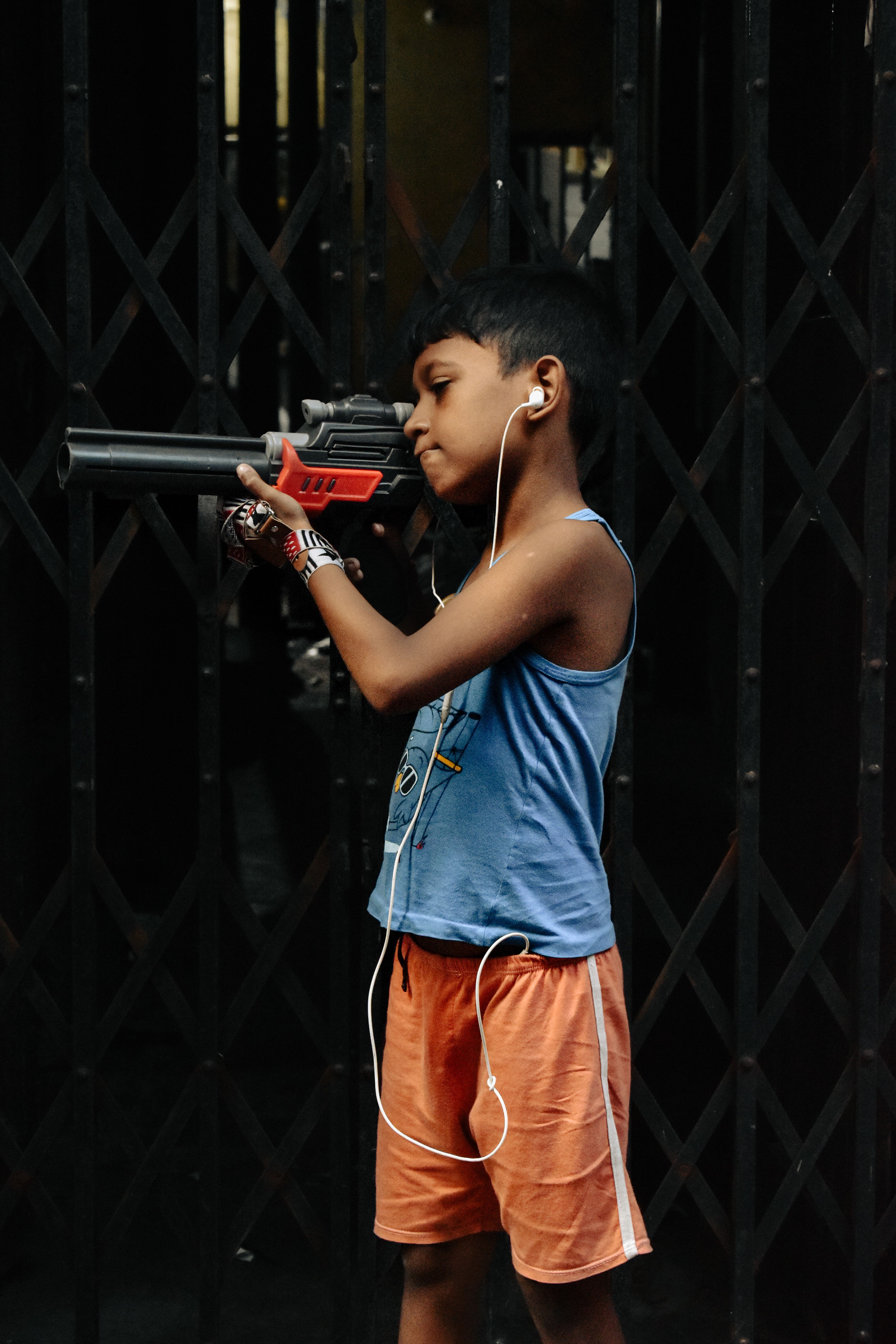 Young boy in tank top listening to music while holding a toy gun.
