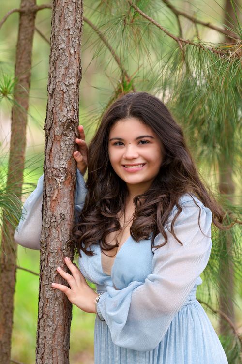 Free A smiling woman poses gracefully in a blue dress surrounded by forest greenery. Stock Photo