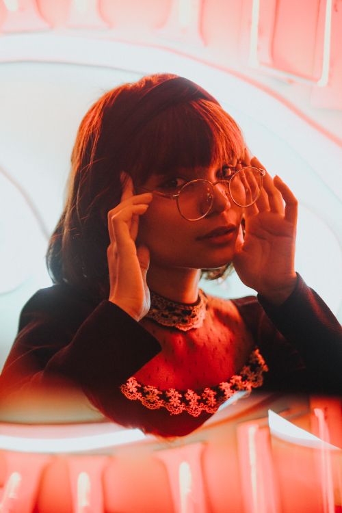 Free Artistic portrait of a woman with eyeglasses in a studio with red neon lighting. Stock Photo