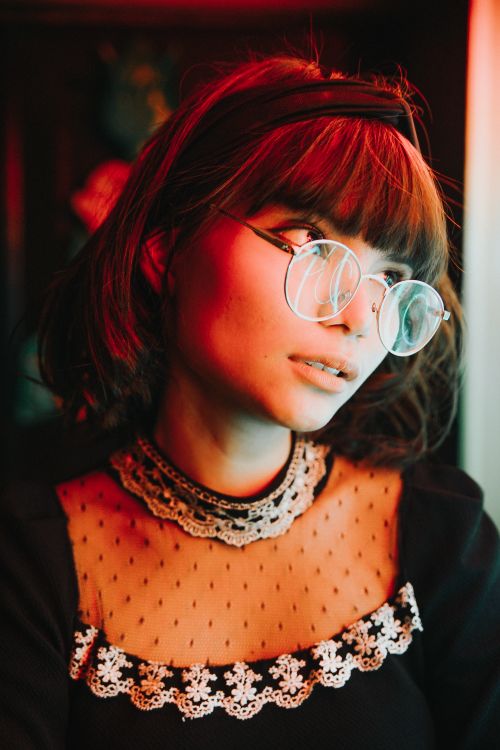 Free A young woman with glasses poses in a stylish outfit under artistic lighting. Stock Photo